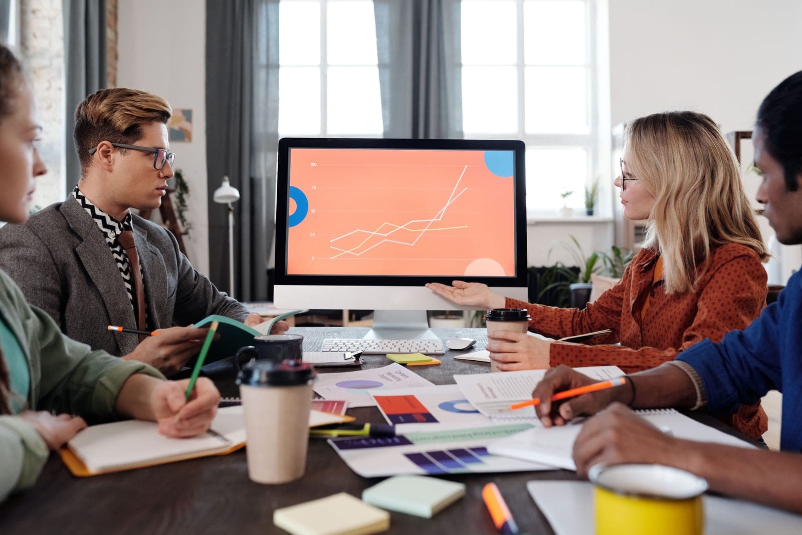 Une équipe échange autour d'un écran affichant un graphique, documents et notes étalés sur la table.